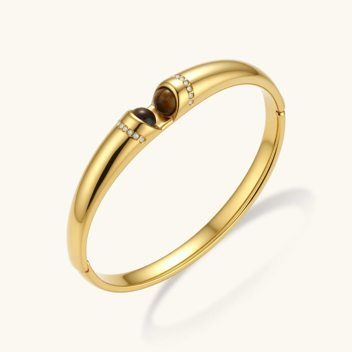 Polished gold bangle with two oval tiger's eye cabochons flanked by pavé diamond accents at center clasp.